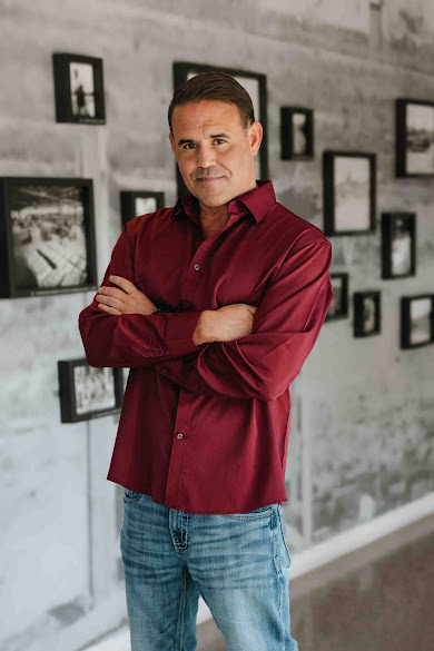 John Strickland in a burgundy shirt, standing with arms folded